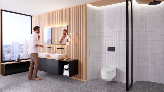 Man in bathroom standing in front of the bathroom mirror and black bathroom furniture (© Geberit) Man in bathroom standing in front of the bathroom mirror and black bathroom furniture (© Geberit)
